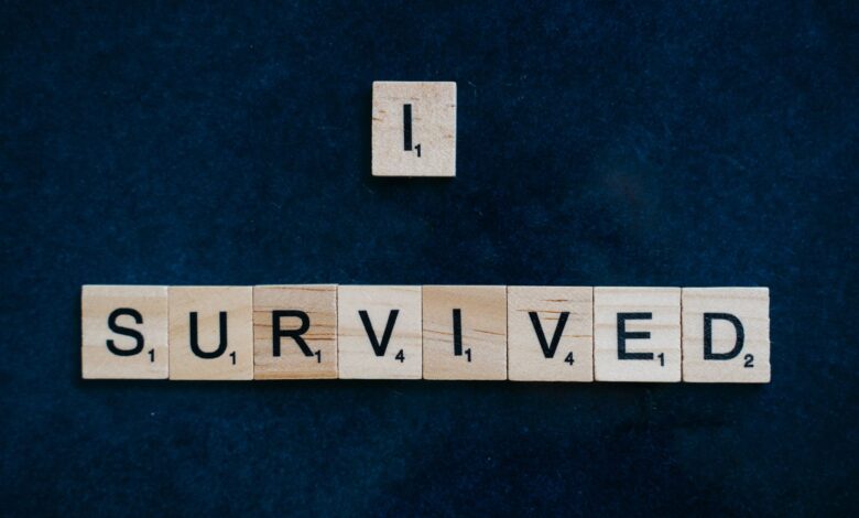 Wooden Scrabble tiles spelling 'I Survived' on a dark surface conveying strength and resilience.