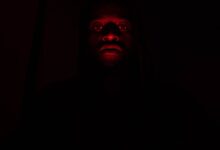 A dramatic portrait of a man illuminated by red light in complete darkness, creating a mysterious effect.