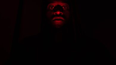 A dramatic portrait of a man illuminated by red light in complete darkness, creating a mysterious effect.