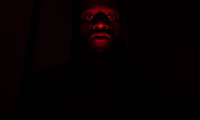 A dramatic portrait of a man illuminated by red light in complete darkness, creating a mysterious effect.