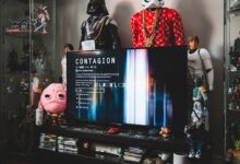 Desktop computer with creative video game on screen near assorted toy superheros on glass shelves in modern style apartment