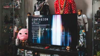 Desktop computer with creative video game on screen near assorted toy superheros on glass shelves in modern style apartment