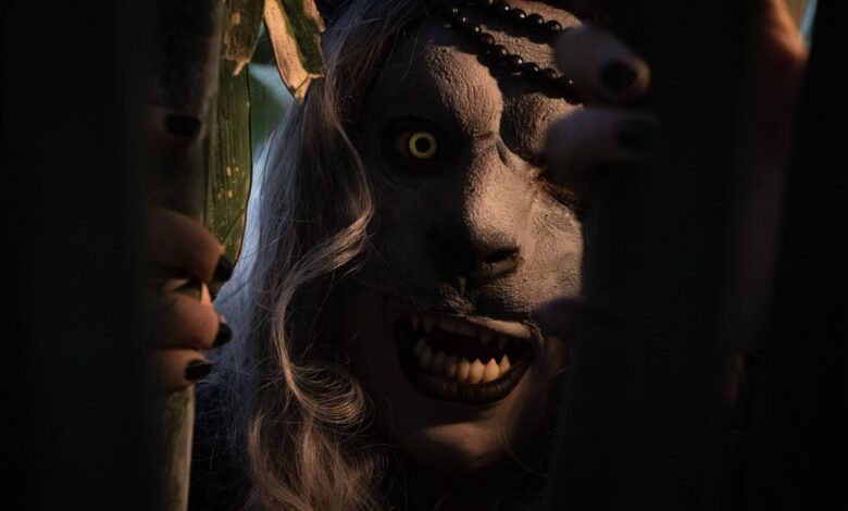 A frightening costumed figure peers through shadows with glowing eyes and sharp teeth, evoking terror in a dark, mysterious setting.