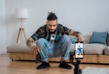 A young man focuses on a bottle flip challenge while filming content at home, capturing it on a smartphone.