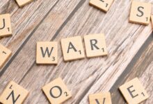 Close-up of wooden scrabble tiles spelling 'WAR' on a wooden background.