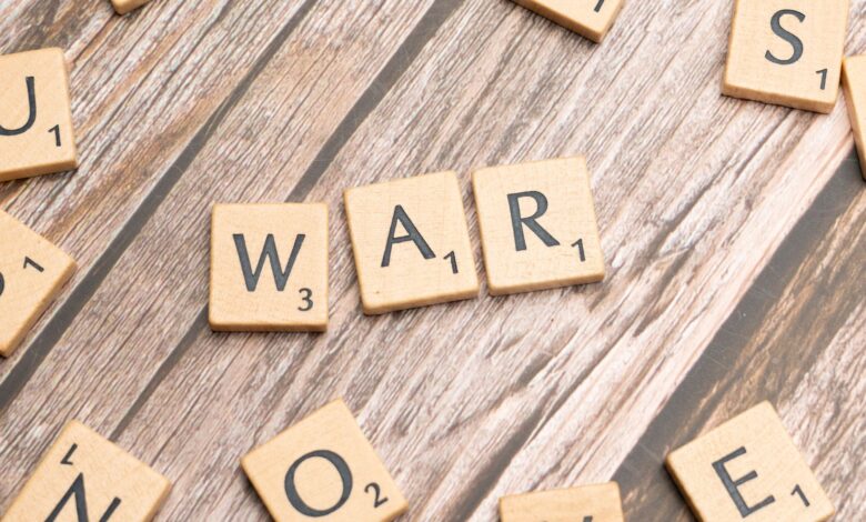 Close-up of wooden scrabble tiles spelling 'WAR' on a wooden background.