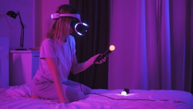 A woman kneels on a bed playing with a VR headset and controllers in a purple-lit room.