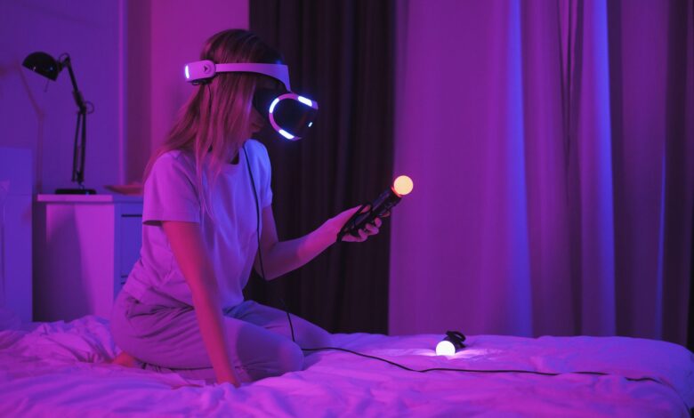 A woman kneels on a bed playing with a VR headset and controllers in a purple-lit room.