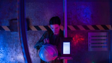 A female astronaut in a spacesuit examines her helmet in a dimly lit spaceship interior.
