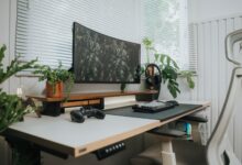 A stylish home office setup with a curved monitor, keyboard, and green plants.