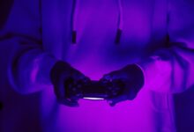 Focused gamer in hoodie holding a PlayStation controller under purple light, creating a vibrant gaming vibe.