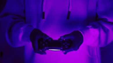 Focused gamer in hoodie holding a PlayStation controller under purple light, creating a vibrant gaming vibe.