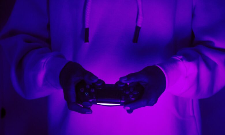 Focused gamer in hoodie holding a PlayStation controller under purple light, creating a vibrant gaming vibe.