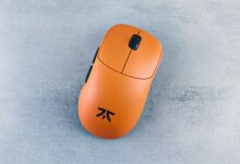 Orange computer mouse on a textured gray surface, showcased simply and artistically.