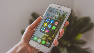 Close-up of a hand holding a smartphone displaying popular social media apps.