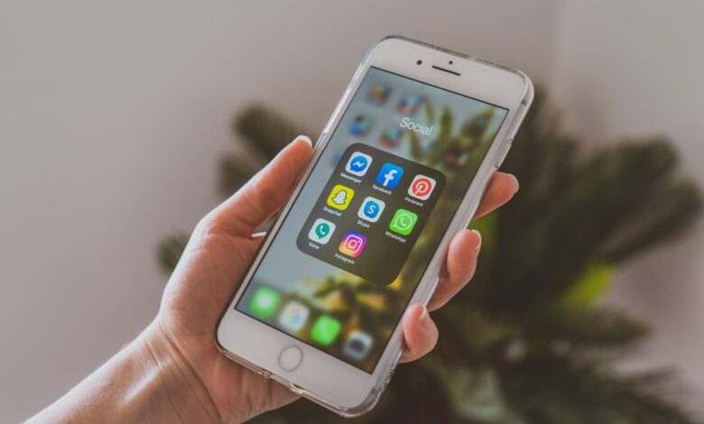 Close-up of a hand holding a smartphone displaying popular social media apps.