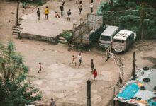 Aerial view of children playing basketball on a street court surrounded by vehicles and urban structures.