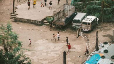 Aerial view of children playing basketball on a street court surrounded by vehicles and urban structures.