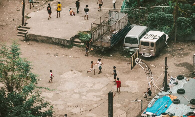 Aerial view of children playing basketball on a street court surrounded by vehicles and urban structures.