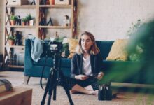 Woman filming vlog at home with camera setup, surrounded by plants and cozy decor.