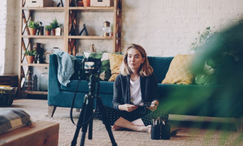 Woman filming vlog at home with camera setup, surrounded by plants and cozy decor.