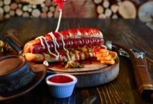 Close-up of a mouth-watering hot dog with ketchup, mayonnaise, and pickles, served on a wooden plate.