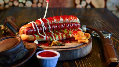 Close-up of a mouth-watering hot dog with ketchup, mayonnaise, and pickles, served on a wooden plate.