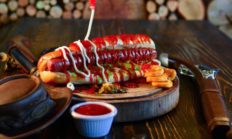 Close-up of a mouth-watering hot dog with ketchup, mayonnaise, and pickles, served on a wooden plate.