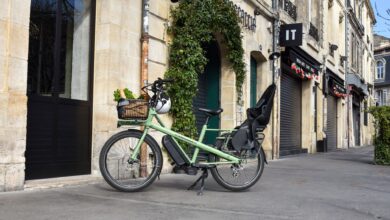 A green cargo e-bike with groceries parked outside a French building on a sunny day.