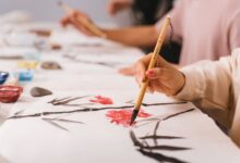 Detailed shot of hands practicing traditional Asian brush painting with vibrant colors, indoors.