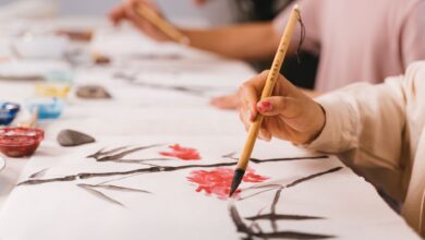 Detailed shot of hands practicing traditional Asian brush painting with vibrant colors, indoors.