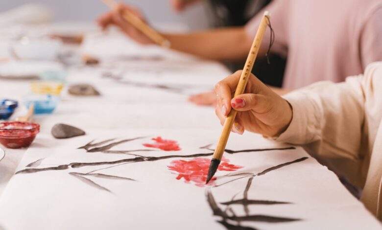 Detailed shot of hands practicing traditional Asian brush painting with vibrant colors, indoors.
