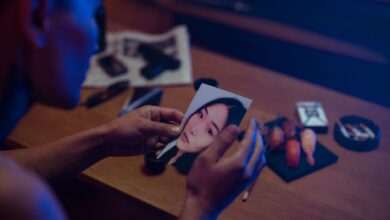 A person holds a photo in a dimly lit room, surrounded by objects suggesting mystery.