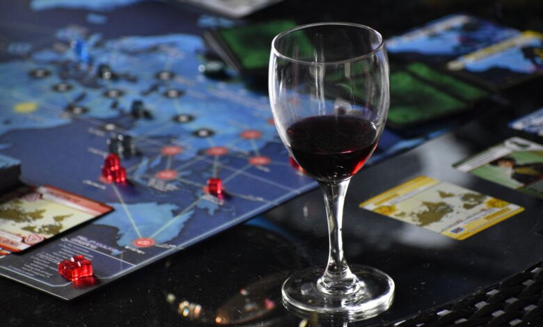 Elegant glass of red wine beside a strategic board game setup on a table.