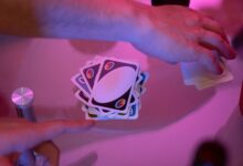 Close-up of hands engaged in a game of cards with vibrant lighting on a table.