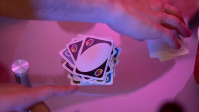 Close-up of hands engaged in a game of cards with vibrant lighting on a table.