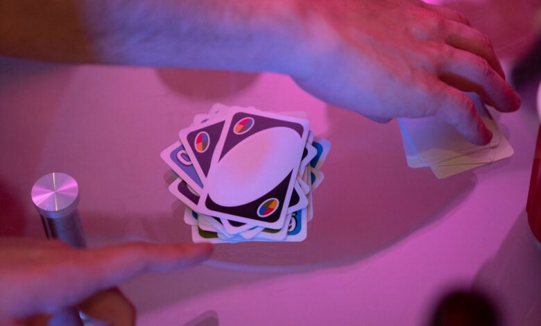 Close-up of hands engaged in a game of cards with vibrant lighting on a table.
