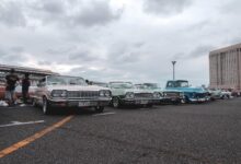 Vintage cars in a parking lot under a cloudy sky, showcasing a classic car meetup.