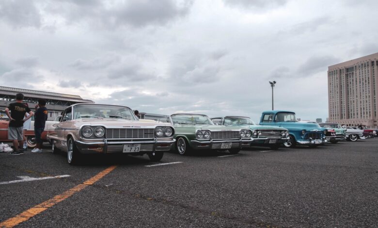 Vintage cars in a parking lot under a cloudy sky, showcasing a classic car meetup.