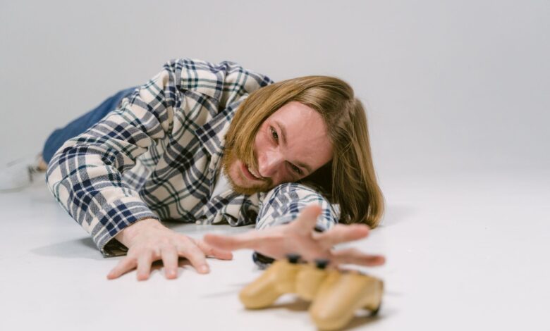 Man in plaid shirt reaching out to grab a gaming controller on a studio floor.