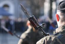 Military personnel holding rifle with bayonet during an outdoor ceremonial event.