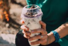 Close-up of hands holding a creamy dessert beverage outdoors, showcasing a refreshing treat.
