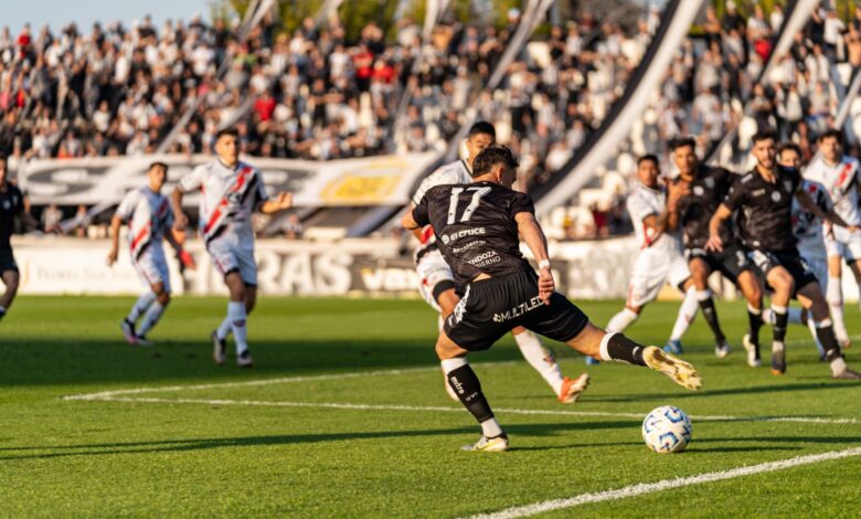A dynamic football match with players in motion on a sunny day, witnessed by a packed stadium.