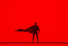 Artistic silhouette of a person with a flowing cape against a vivid red backdrop, creating a dramatic effect.