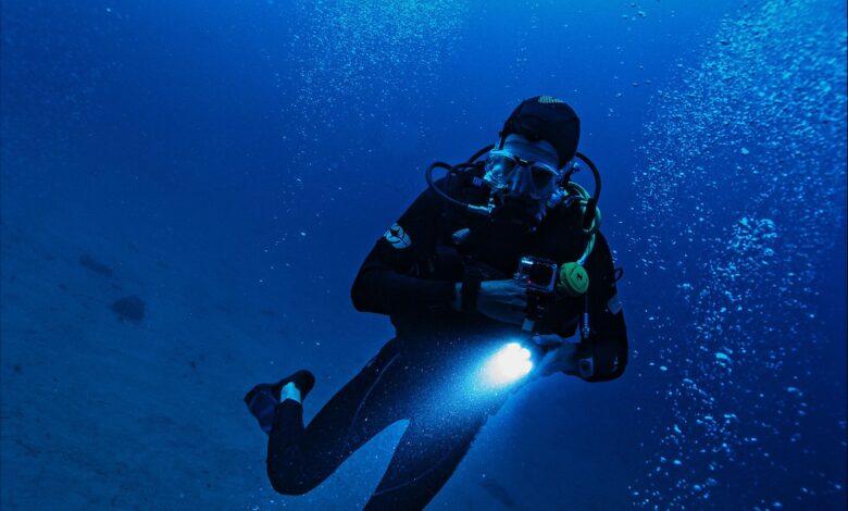 A scuba diver exploring the deep ocean with a flashlight, surrounded by bubbles and marine life.