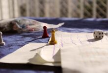 Close-up of colorful game pawns and a dice on a paper board under sunlight.