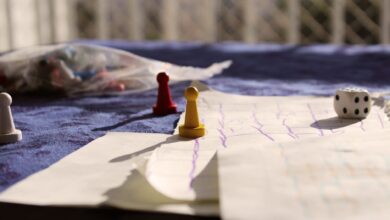 Close-up of colorful game pawns and a dice on a paper board under sunlight.