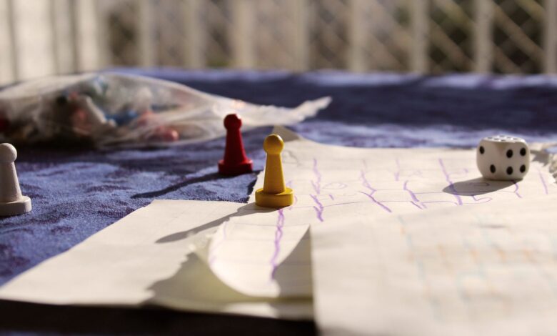 Close-up of colorful game pawns and a dice on a paper board under sunlight.
