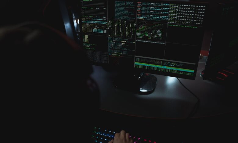 Dark room setup with code displayed on PC monitors highlighting cybersecurity themes.