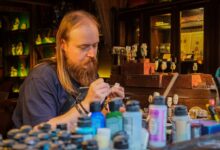 Skilled artisan meticulously painting miniatures in a cozy, cluttered workshop with various vibrant paints.